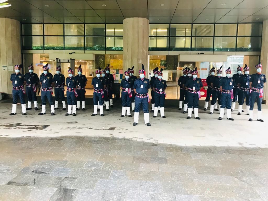 A full detachment of Industrial Security Force guards in ceremonial uniform fallen in outside a corporate building lobby